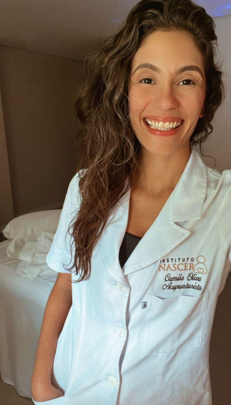 Camila Oliva sorrindo, de jaleco do Instituto Nascer, na sala de atendimento